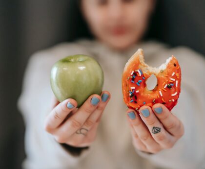 woman showing apple and bitten doughnut